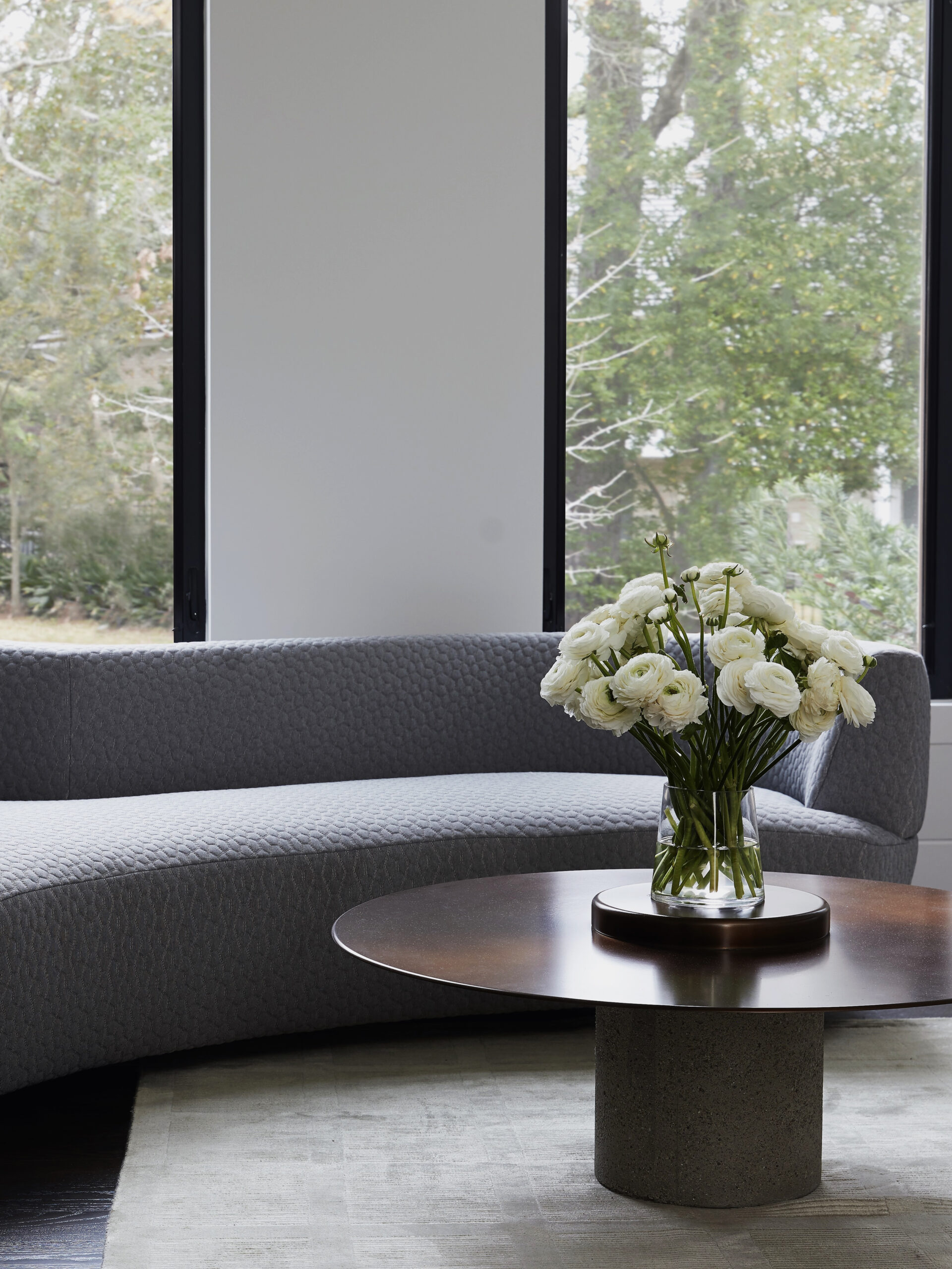 Elegant primary bedroom seating area in a Houston home by Nina Magon featuring a textured gray sofa and modern round table with fresh florals.