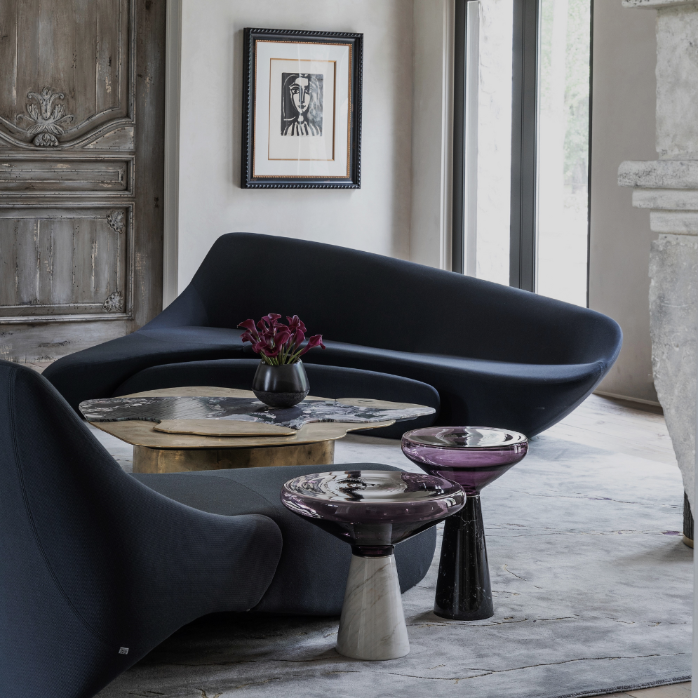 Memorial residence by Nina Magon Studio featuring a sculptural midnight-blue curved sofa, artisanal stone side tables, a marble fireplace, and historic wooden doors layered with gallery artwork.