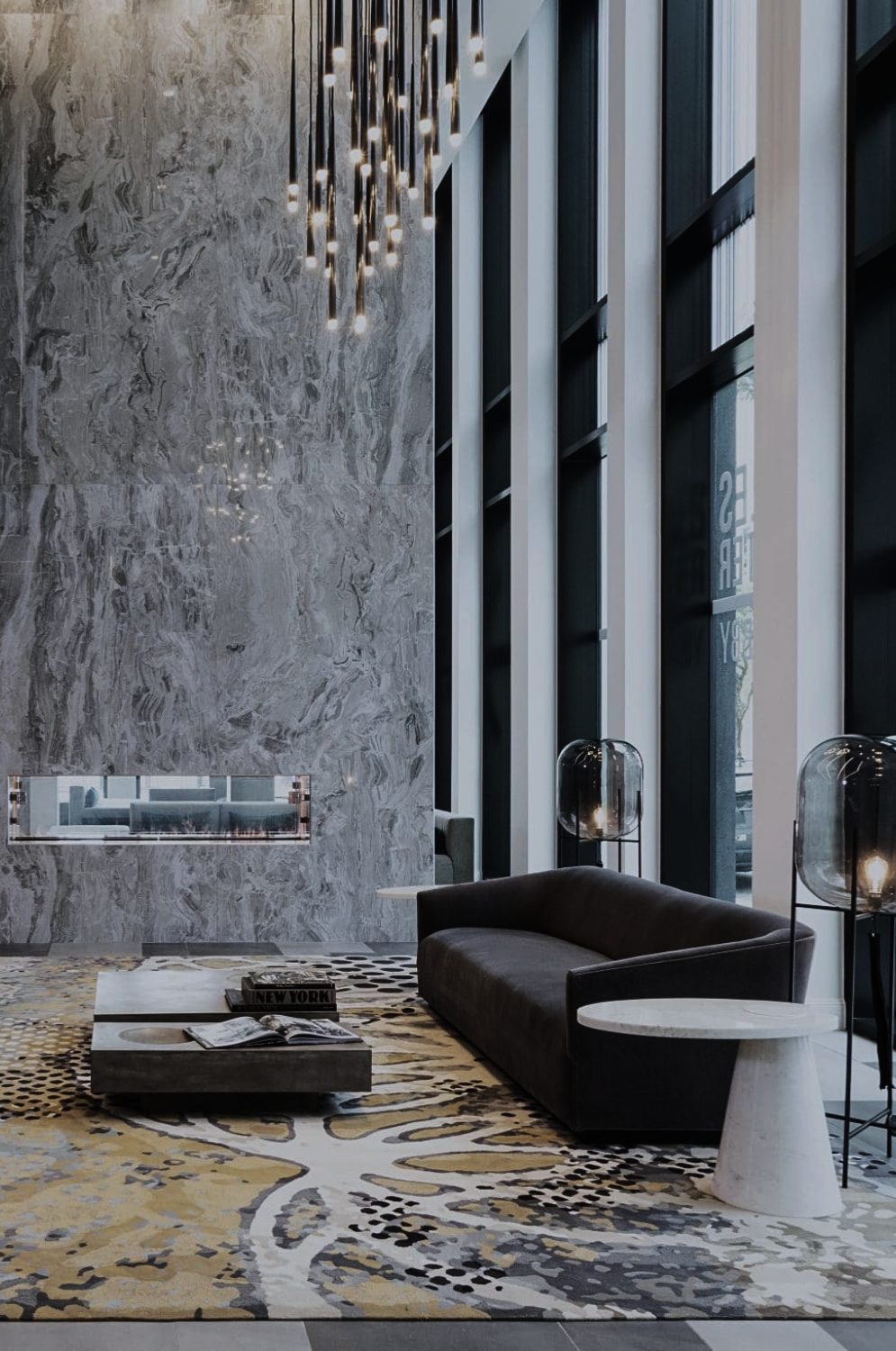 Marlowe hospitality lounge by Nina Magon Studio featuring a sculptural chandelier, marble fireplace wall, and a custom patterned rug in a modern luxury interior.