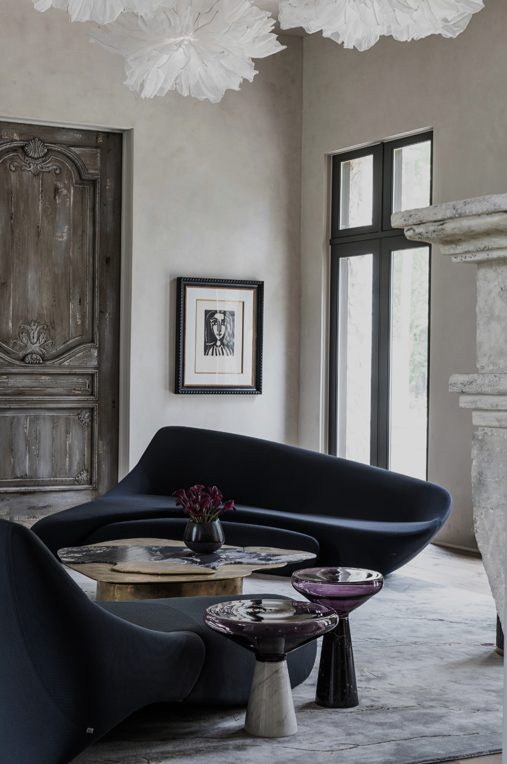 Memorial residence by Nina Magon Studio featuring a sculptural midnight-blue curved sofa, artisanal stone side tables, a marble fireplace, and historic wooden doors layered with gallery artwork.