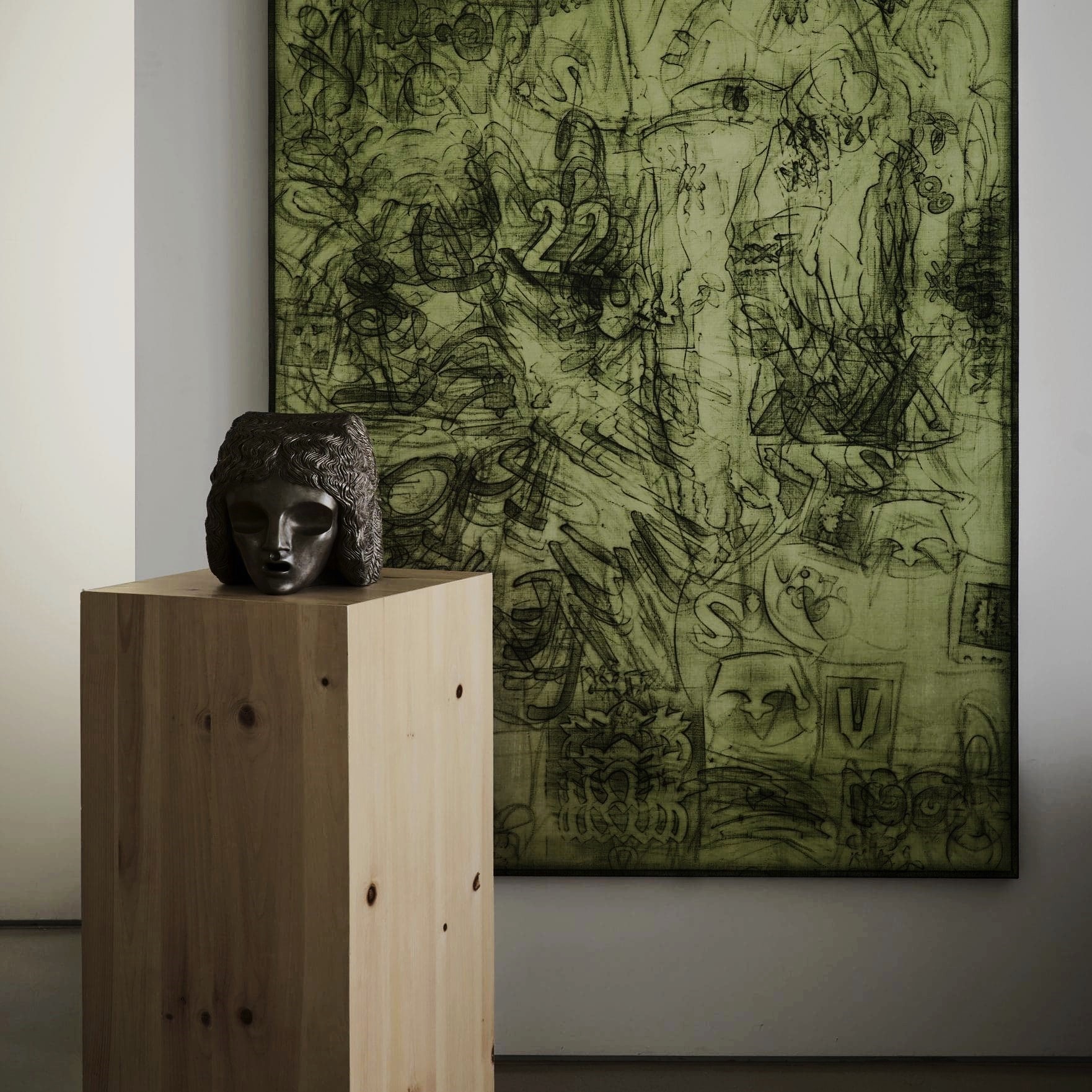 Nina Magon interior vignette with a carved stone head sculpture displayed on a light wood pedestal in front of a large green abstract artwork