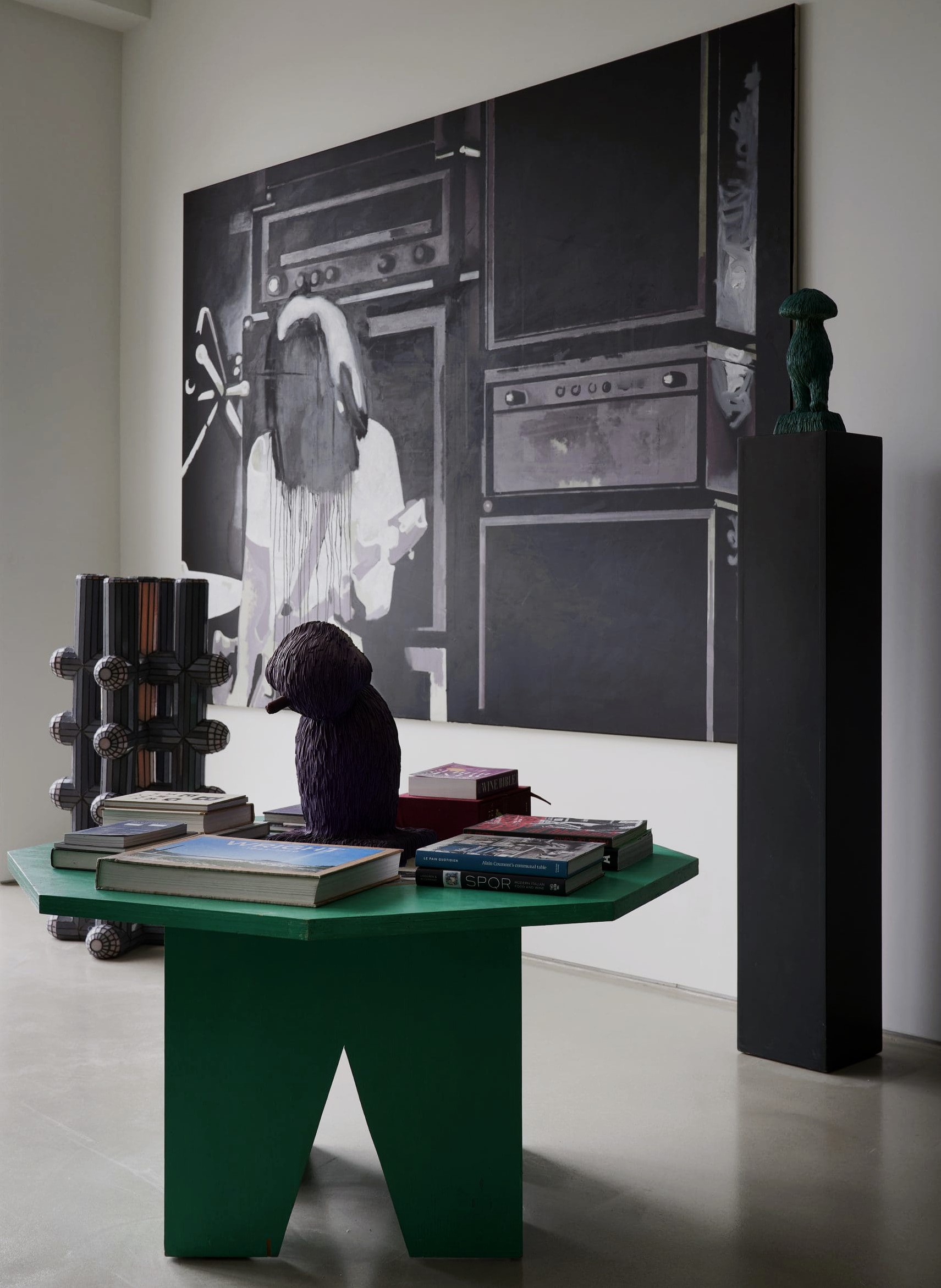 Nina Magon interior vignette featuring a sculptural green table styled with books and objects beneath a large black-and-white artwork